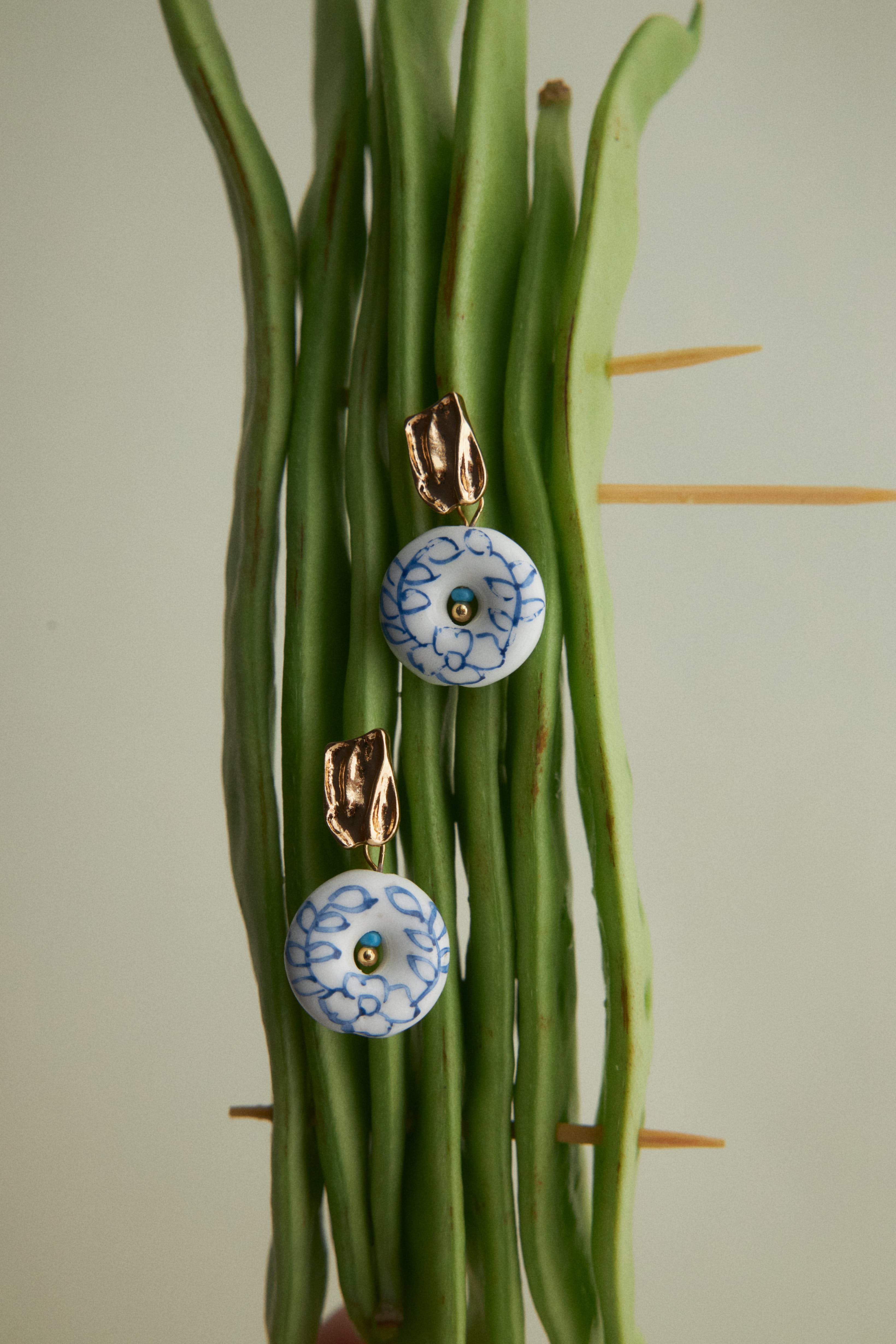 Pair of earrings with blue floral designs hanging on green stems.
