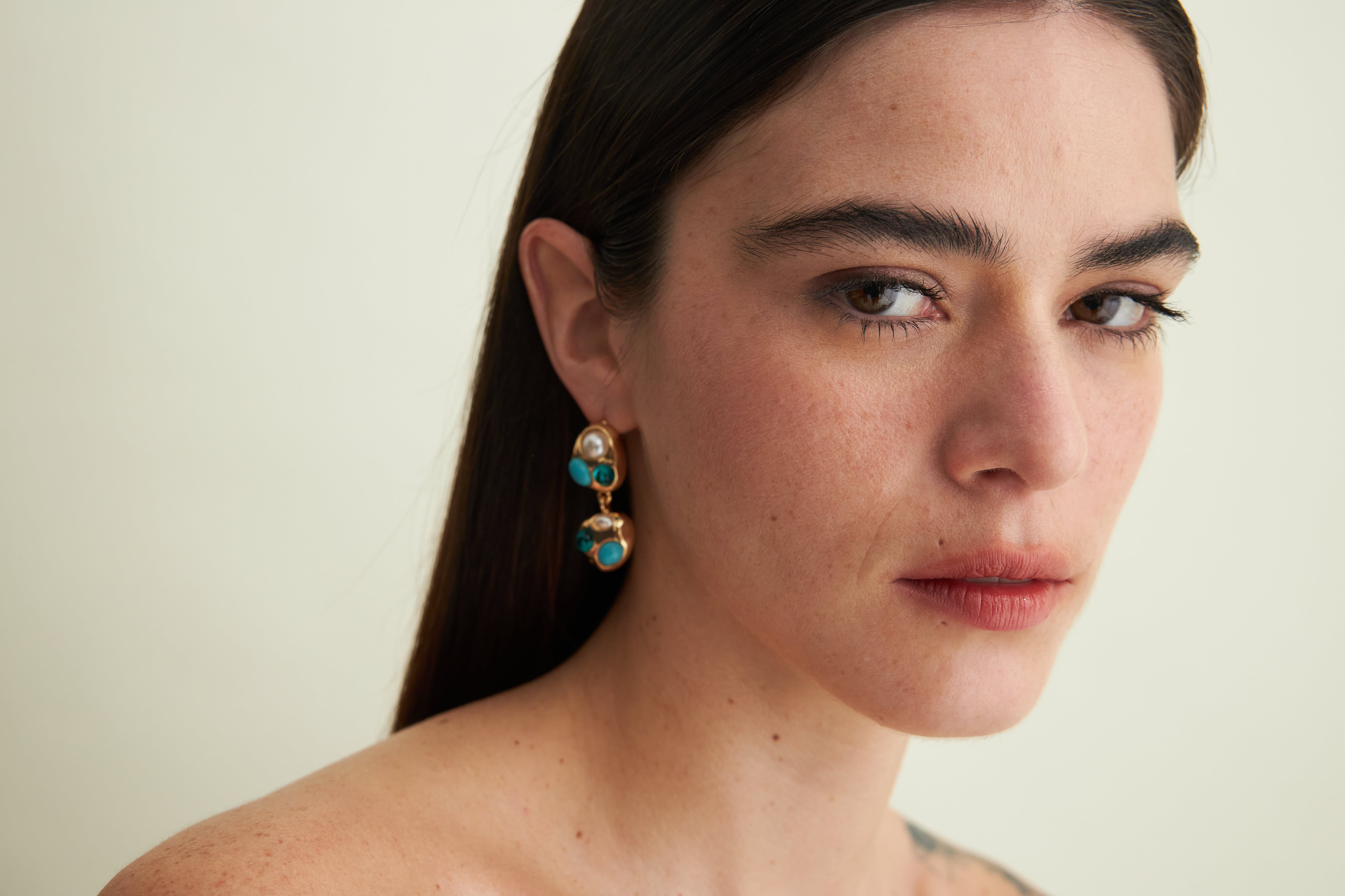 Woman wearing gold earrings with turquoise stones against a neutral background